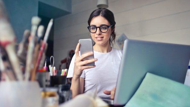 woman at her desk with art supplies on her phone