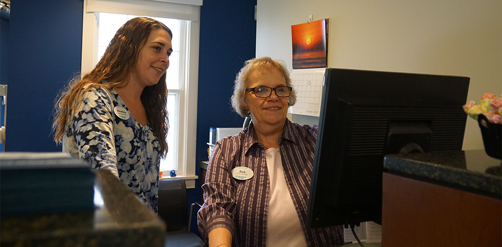 Two coworkers look at a document on a computer screen.