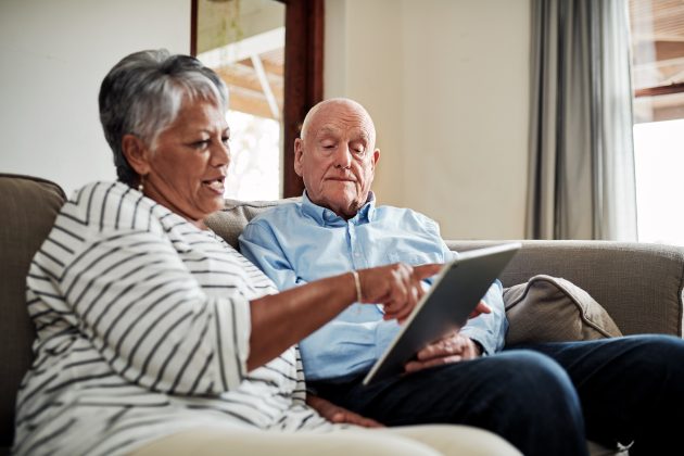 senior couple on couch looking at a tablet